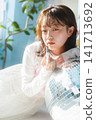 A young woman, holding lipstick in the light, gazes with an ennui expression. 141713692