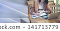 Asian Female freelance using laptop at home office desk. Woman reading financial graph chart Planning analyzing marketing data. Asian female people working office firm with business stuff, coffee cup 141713779