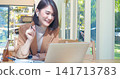 Happy asian woman video call web conference sitting on cozy sofa in living room at home. Smile Female asian people use laptop notebook computer headphones online call working from home watching video 141713783