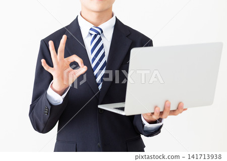 一位身穿西裝的年輕商務人士手持筆記型電腦,做著畫圈的動作。 一位身穿西裝的年輕商務人士手持筆記型電腦,做著畫圈的動作。 141713938