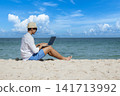 Man traveler use laptop on summer beach blue sky. Asian man casual blue short pants white shirt relax sitting summer beach. Man typing laptop computer holiday business trip freelance work on island 141713992