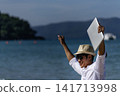 Man traveler use laptop on summer beach blue sky. Asian man wear casual short pants tropical shirt style relax on the beach in summertime. Man typing laptop computer  holiday business trip 141713998