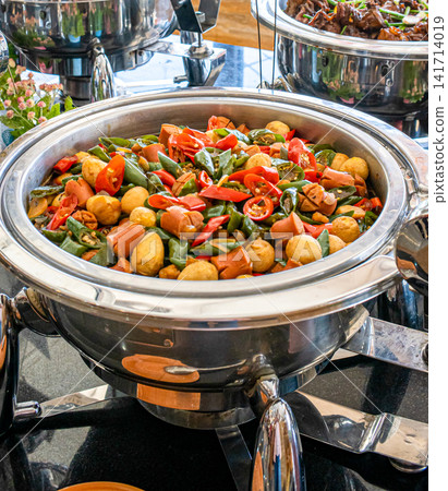 Authentic Indonesian stir fried sausage and quail eggs with green chilies presented in buffet serving tray. Asian spicy cuisine for catering, restaurants, hotels and culinary concepts. Authentic Indonesian stir fried sausage and quail eggs with green chilies presented in buffet serving tray. Asian spicy cuisine for catering, restaurants, hotels and culinary concepts. 141714019