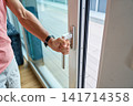 Man Opening Large Glass Door to Terrace 141714358