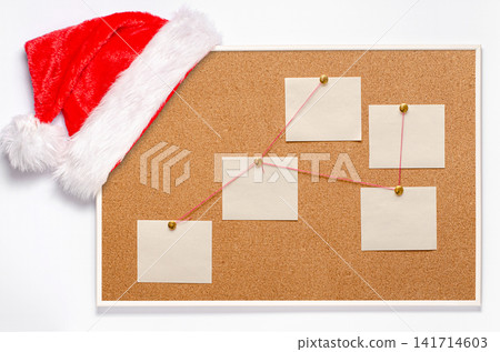 Blank note sheets are pinned to the board. Santa's hat on a cork board. Blank note sheets are pinned to the board. Santa's hat on a cork board. 141714603