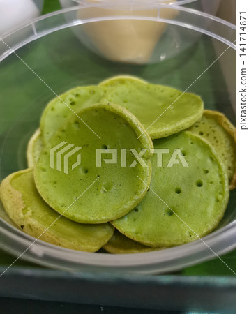 Traditional Indonesian pandan rice pancakes packed in a clear takeaway container. Authentic Southeast Asian snack suitable for restaurant, food delivery, travel, hospitality, and culinary projects. Traditional Indonesian pandan rice pancakes packed in a clear takeaway container. Authentic Southeast Asian snack suitable for restaurant, food delivery, travel, hospitality, and culinary projects. 141714871