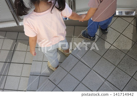 The backs of children walking down the outdoor stairs hand in hand. The backs of children walking down the outdoor stairs hand in hand. 141714942