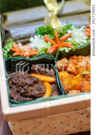 Traditional Indonesian food hamper featuring authentic beef rendang and spicy kentang balado served in banana leaf containers inside a woven bamboo basket for Ramadan, Eid and catering. Traditional Indonesian food hamper featuring authentic beef rendang and spicy kentang balado served in banana leaf containers inside a woven bamboo basket for Ramadan, Eid and catering. 141714981
