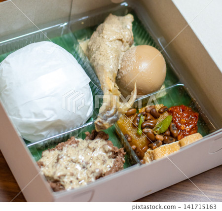 Indonesian gudeg rice meal served in a takeaway box with sweet jackfruit, chicken, braised egg, tofu, beans and spicy sambal, showcasing traditional Yogyakarta cuisine and local food culture. Indonesian gudeg rice meal served in a takeaway box with sweet jackfruit, chicken, braised egg, tofu, beans and spicy sambal, showcasing traditional Yogyakarta cuisine and local food culture. 141715163