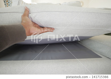 Person lifting a couch cushion to reveal storage space Person lifting a couch cushion to reveal storage space 141715366