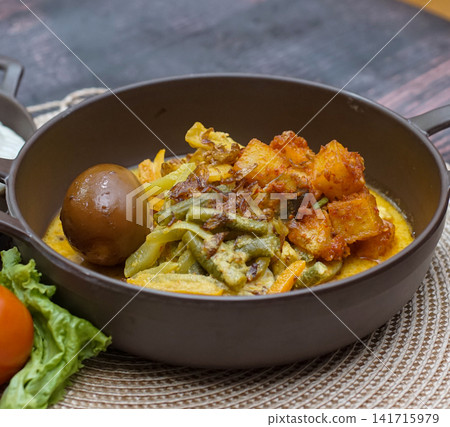 Indonesian lontong sayur with rice cake, vegetables, tofu, and egg in coconut curry. Traditional Asian dish with authentic taste and colorful presentation. Indonesian lontong sayur with rice cake, vegetables, tofu, and egg in coconut curry. Traditional Asian dish with authentic taste and colorful presentation. 141715979