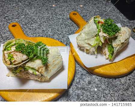 Fresh chicken tortilla wrap with lettuce and parsley served on wooden board in kitchen healthy homemade meal. Fresh chicken tortilla wrap with lettuce and parsley served on wooden board in kitchen healthy homemade meal. 141715985