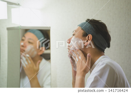 一名 40 歲的男子在晨間護膚程序中,對著三面鏡塗抹洗面乳。 一名 40 歲的男子在晨間護膚程序中,對著三面鏡塗抹洗面乳。 141716424
