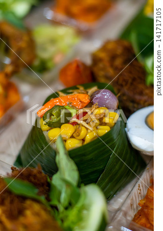 Traditional Indonesian Nasi Tempong featuring banana leaf rice, Ayam Goreng Laos, salted egg, sambal, anchovies and colorful vegetables. Authentic Banyuwangi culinary specialty. Traditional Indonesian Nasi Tempong featuring banana leaf rice, Ayam Goreng Laos, salted egg, sambal, anchovies and colorful vegetables. Authentic Banyuwangi culinary specialty. 141717105