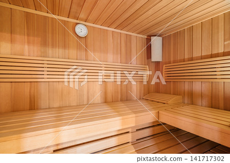 Wooden sauna interior with tiered benches, round wall clock, slatted timber walls, and warm amber light creating calm wellness retreat for relaxation, comfort, and serene spa atmosphere Wooden sauna interior with tiered benches, round wall clock, slatted timber walls, and warm amber light creating calm wellness retreat for relaxation, comfort, and serene spa atmosphere 141717302