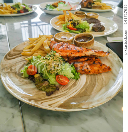 Grilled salmon with fresh salad and fries served on plate. Healthy western style meal with balanced nutrition. Grilled salmon with fresh salad and fries served on plate. Healthy western style meal with balanced nutrition. 141717633
