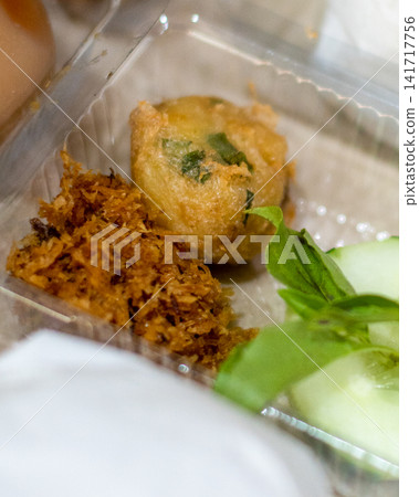 Traditional Indonesian perkedel and serundeng served in a takeaway catering meal box with cucumber and basil. Authentic Southeast Asian side dishes for restaurant, catering, and food delivery concepts Traditional Indonesian perkedel and serundeng served in a takeaway catering meal box with cucumber and basil. Authentic Southeast Asian side dishes for restaurant, catering, and food delivery concepts 141717756