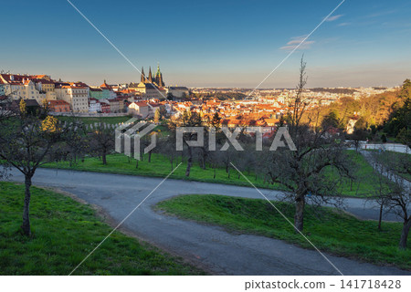 Panoramic Prague cityscape from Petrin Hill with historic red rooftops, green orchards and cathedral towers, capturing scenic spring views of Prague City Czech Republic under clear blue sky Panoramic Prague cityscape from Petrin Hill with historic red rooftops, green orchards and cathedral towers, capturing scenic spring views of Prague City Czech Republic under clear blue sky 141718428