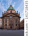 Historic Church of Saint Francis of Assisi with green Baroque dome in Prague City Czech Republic, showcasing ornate European architecture and a peaceful cobblestone square beneath a blue sky 141718435