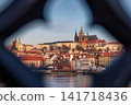 Prague Castle and Saint Vitus Cathedral framed through historic bridge architecture across the Vltava River, revealing iconic red rooftops and the timeless skyline of Prague City Czech Republic 141718436
