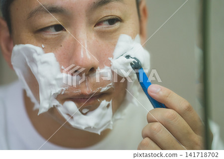 Men's grooming: A man in his 40s carefully shaves his cheeks using shaving foam. Men's grooming: A man in his 40s carefully shaves his cheeks using shaving foam. 141718702