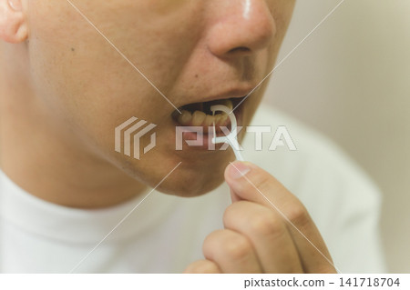 Oral care of a man in his 40s who carefully cleans between his teeth with a dental floss pick. Oral care of a man in his 40s who carefully cleans between his teeth with a dental floss pick. 141718704