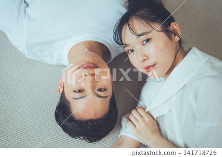 一張俯拍的肖像照,一對恩愛的情侶面帶微笑,依偎在地毯上,抬頭看著鏡頭。 一張俯拍的肖像照,一對恩愛的情侶面帶微笑,依偎在地毯上,抬頭看著鏡頭。 141718726
