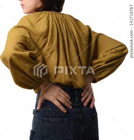 Asian woman wearing mustard blouse shows hand placement across lower back with dark denim garment on isolated background Asian woman wearing mustard blouse shows hand placement across lower back with dark denim garment on isolated background 141718767
