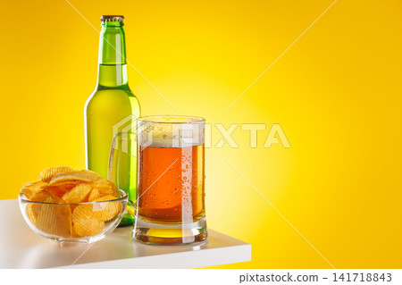 Beer mug with foam chips and bottle on yellow background snack setup Beer mug with foam chips and bottle on yellow background snack setup 141718843