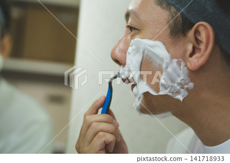 Morning routine for a man in his 40s: Applying shaving foam and carefully shaving the facial hair around his mouth. Morning routine for a man in his 40s: Applying shaving foam and carefully shaving the facial hair around his mouth. 141718933