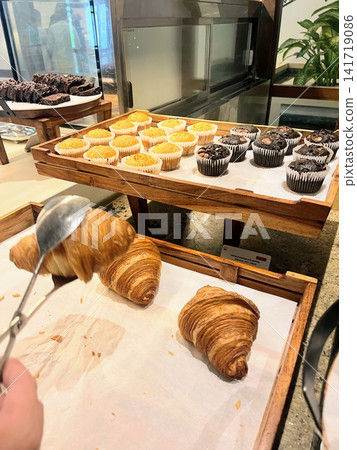 自助餐檯上擺放著羊角麵包、鬆餅和布朗尼蛋糕,人們用夾子夾取這些食物。 自助餐檯上擺放著羊角麵包、鬆餅和布朗尼蛋糕,人們用夾子夾取這些食物。 141719086