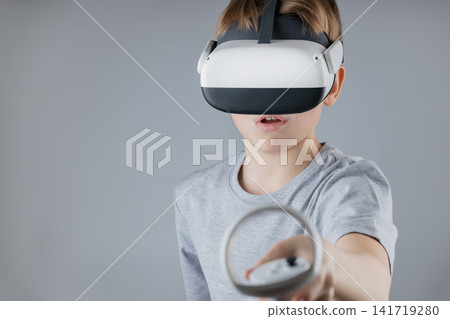 Kid Gamer in Serene Gray Tee Experiencing Futuristic VR World, Holding Controllers and Wearing Headset Enthusiastically Kid Gamer in Serene Gray Tee Experiencing Futuristic VR World, Holding Controllers and Wearing Headset Enthusiastically 141719280