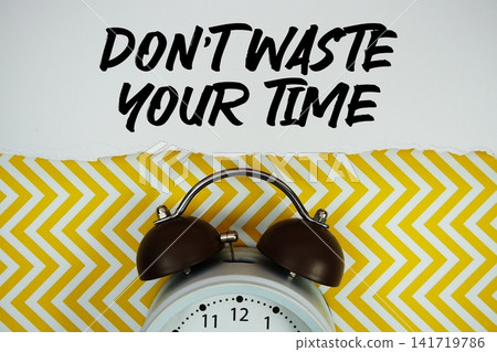 Don't Waste Your Time text written on paper with alarm clock on yellow chevron background Don't Waste Your Time text written on paper with alarm clock on yellow chevron background 141719786