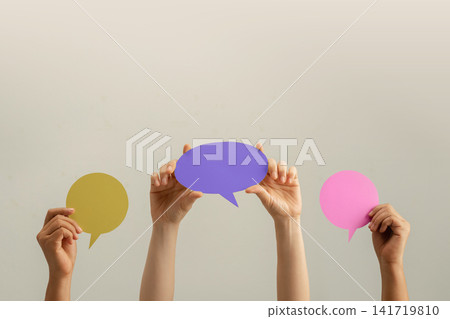 Raised hands hold colorful speech bubbles against a plain background 141719810