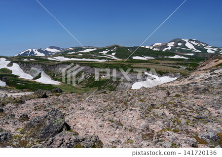 A stunning summer scene: The snow-covered ridge trail from Mt. Akadake to Mt. Hakuunzan in Hokkaido's Daisetsuzan Mountains. A stunning summer scene: The snow-covered ridge trail from Mt. Akadake to Mt. Hakuunzan in Hokkaido's Daisetsuzan Mountains. 141720136