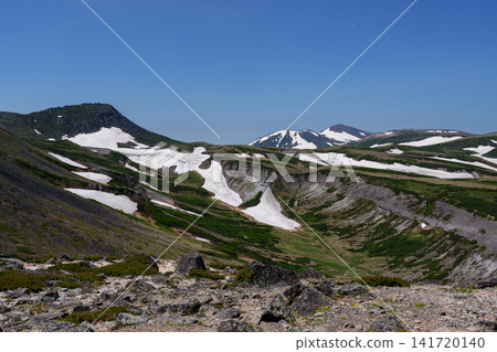 A stunning summer scene: The snow-covered ridge trail from Mt. Akadake to Mt. Hakuunzan in Hokkaido's Daisetsuzan Mountains. A stunning summer scene: The snow-covered ridge trail from Mt. Akadake to Mt. Hakuunzan in Hokkaido's Daisetsuzan Mountains. 141720140