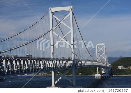 A landscape featuring a blue sky, white clouds, the Naruto Strait Bridge, the blue surface of the sea, ships, mountains, and a coastal townscape. A landscape featuring a blue sky, white clouds, the Naruto Strait Bridge, the blue surface of the sea, ships, mountains, and a coastal townscape. 141720267