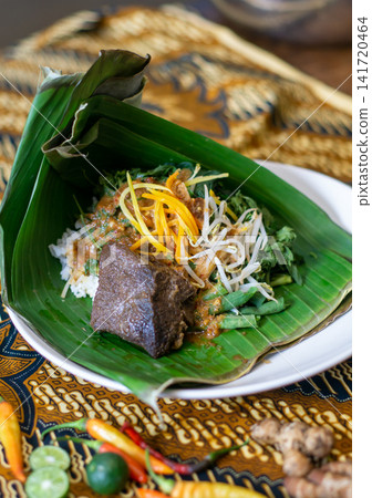 Pecel tahu bacem Indonesian traditional dish with peanut sauce, tofu, vegetables, and rice served on banana leaf. Authentic Asian cuisine concept. Pecel tahu bacem Indonesian traditional dish with peanut sauce, tofu, vegetables, and rice served on banana leaf. Authentic Asian cuisine concept. 141720464