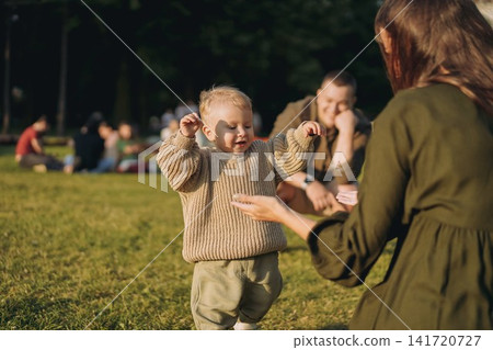 young parents with baby son learning to walk in the park 141720727
