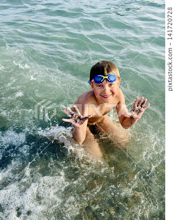 little boy wearing goggles splashing in sea waves happily laughing little boy wearing goggles splashing in sea waves happily laughing 141720728