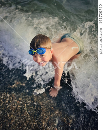 little boy wearing goggles splashing in sea catching waves happily laughing little boy wearing goggles splashing in sea catching waves happily laughing 141720730