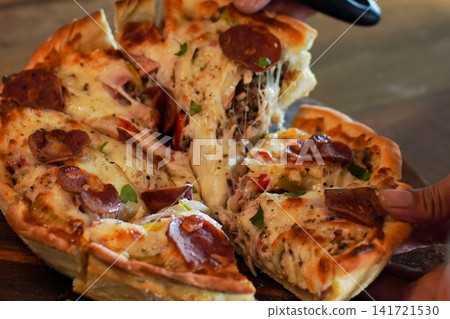 Close-up of hot pepperoni pizza with stretchy melted cheese. Hands pulling slices apart. Comfort food and sharing meal concept. Close-up of hot pepperoni pizza with stretchy melted cheese. Hands pulling slices apart. Comfort food and sharing meal concept. 141721530