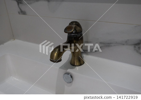 Old brass faucet above a white ceramic sink Old brass faucet above a white ceramic sink 141722919