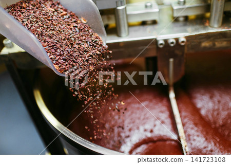 Artisan chocolate making, adding cocoa grits in the Melanger Stone Grinder at home made factory Artisan chocolate making, adding cocoa grits in the Melanger Stone Grinder at home made factory 141723108