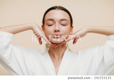 Young woman doing face building yoga self massage with hands. Facial gymnastics and rejuvenating female skin exercises. Spa concept. Young woman doing face building yoga self massage with hands. Facial gymnastics and rejuvenating female skin exercises. Spa concept. 141723115