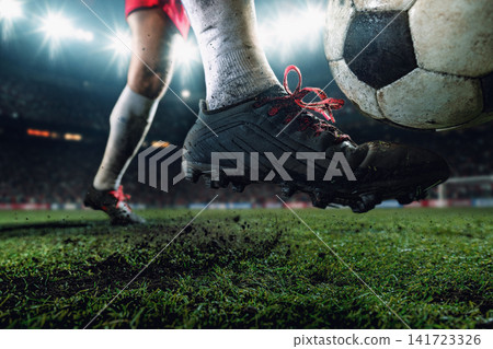 Close-up football boot balancing airborne soccer ball above wet grass under stadium lights Close-up football boot balancing airborne soccer ball above wet grass under stadium lights 141723326
