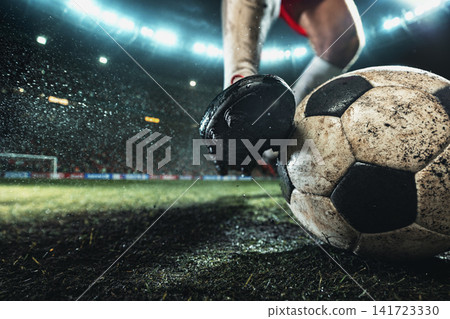 Extreme close-up of black football cleat pressing dirty soccer ball into wet textured grass Extreme close-up of black football cleat pressing dirty soccer ball into wet textured grass 141723330