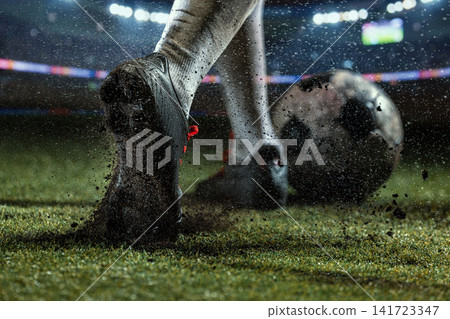 Macro view of mud-caked football studs digging into wet turf beside spinning soccer ball Macro view of mud-caked football studs digging into wet turf beside spinning soccer ball 141723347