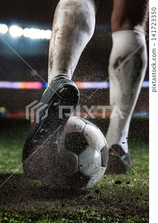 Close-up rear view of muddy football boots controlling worn ball on soaked grass under stadium lights Close-up rear view of muddy football boots controlling worn ball on soaked grass under stadium lights 141723350