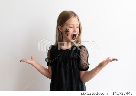 Confused or surprised young girl with Halloween face paint gesturing hands out Confused or surprised young girl with Halloween face paint gesturing hands out 141723443
